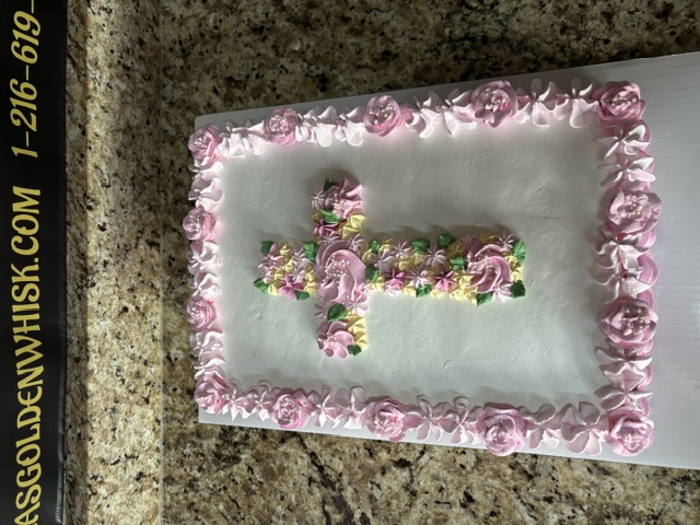 White cake with scattered pink blossoms and a pearl cross