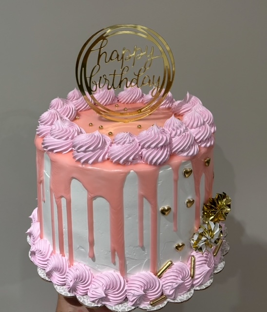 Pink drip cake with swirled piping and gold accents