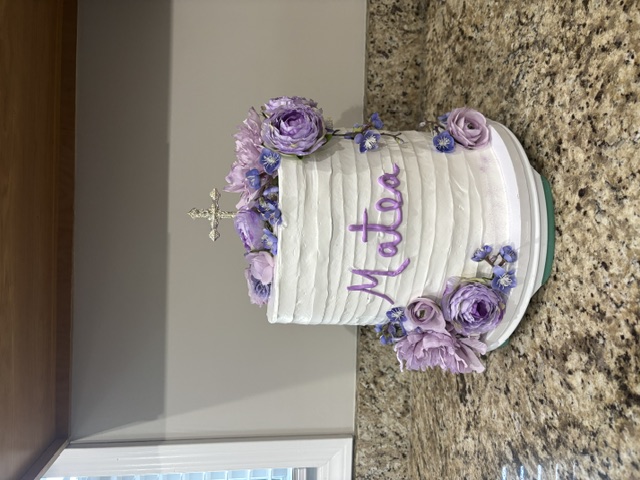 White cake with lavender roses and a silver cross topper