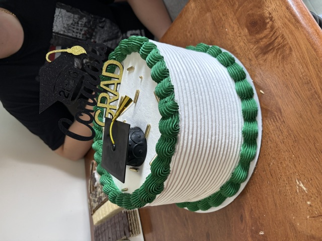 White cake with a green border and a graduation cap topper